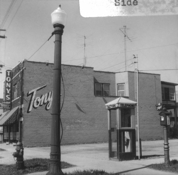 View towards the right side of Tony Urso's Westside Palm Tavern located at 730-736 West Washington Avenue in the Greenbush neighborhood. In the foreground on the left is a fire hydrant and lamppost on the terrace, and on the right near the sidewalk is a telephone booth and a fire box.