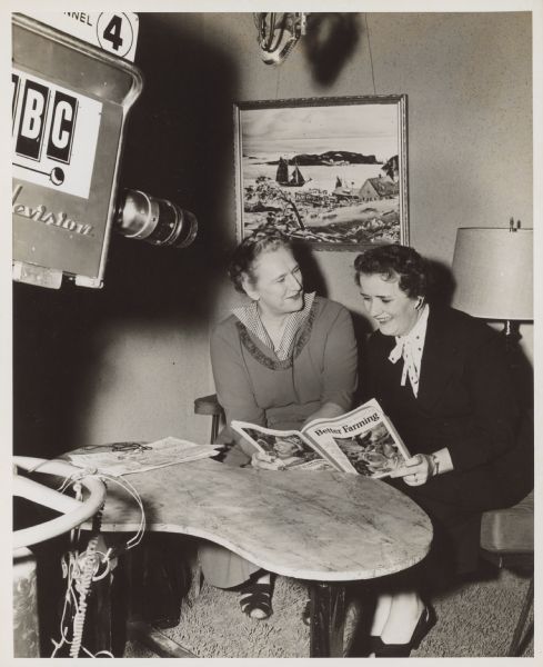 Esther Van Wagoner Tufty is sitting with congresswoman Coya Knutson, who is holding a copy of "Better Farming." A television camera is in the left foreground.
