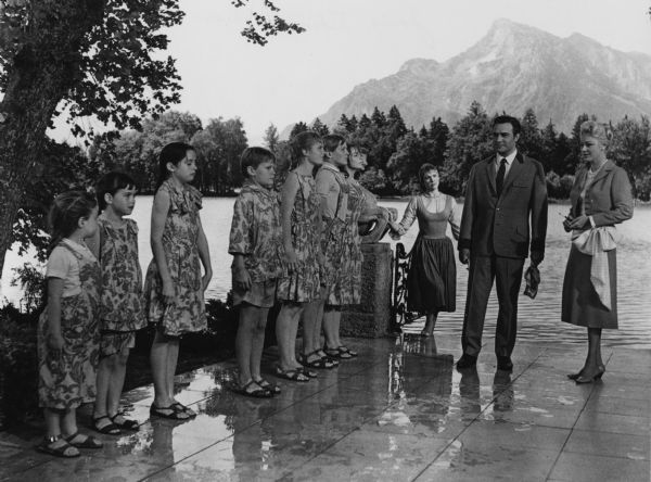 The Von Trapp children stand in a line wearing soaking wet play clothes after capsizing a rowboat. Julie Andrews as the children's governess Maria stands at the edge of the water. Christopher Plummer as Baron von Trapp stands with Eleanor Parker as Baroness Schraeder and looks disapprovingly at the group. Mountains, trees and a lake can be seen in the background.

The children are, from left to right: Kym Karath as Gretl, Debbie Turner as Marta, Angela Cartwright as Brigitta, Duane Chase as Kurt, Heather Menzies as Louisa, Nicholas Hammond as Frederich, and Charmian Carr as Liesl.