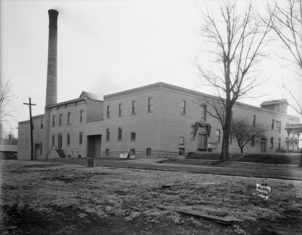 Exterior view of the Blumer Brewery building. Two men are standing in the left background at the corner of the building. The porch of a building is on the far right.