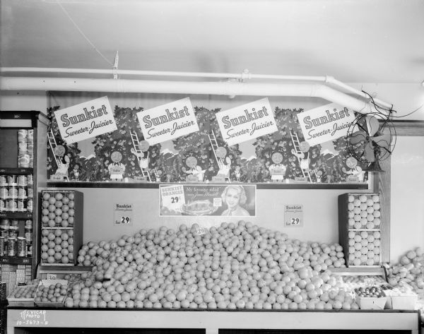 California Fruit Exchange Sunkist oranges display with signs that read: "Sweeter-Juicier" and "Sunkist Oranges 29 cents 'My favorite salad' says Joan Blondell."