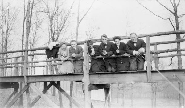 Group portrait of men and women kneeling as if in prayer on a wooden bridge. The photograph was taken by Peter Jacobson, at right, by operating the shutter with a string.