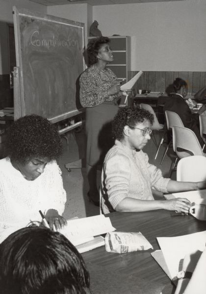 Several women attending a class at the YWCA. The word "Communication" is written on a blackboard.