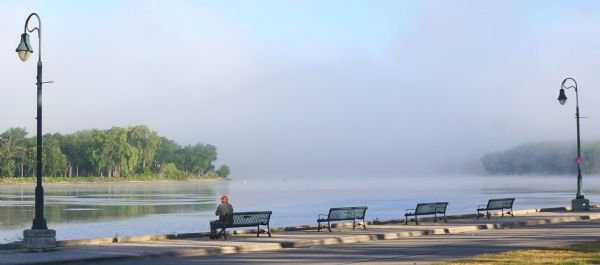 Man viewing fog on the Mississippi River from a bench in Riverside Park.
