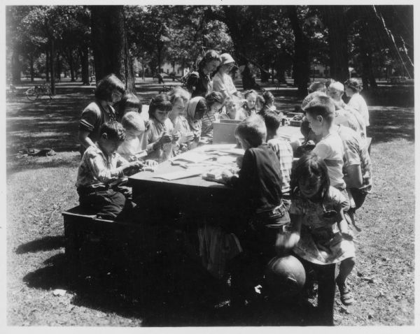 Children, teachers, and a nun sit at a picnic table at the School for Migrants. The school was set up by the Community Council on Human Relations.