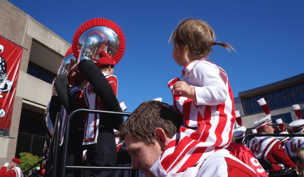 Young Badger fan on shoulders of a man looking at tuba players in the marching band.