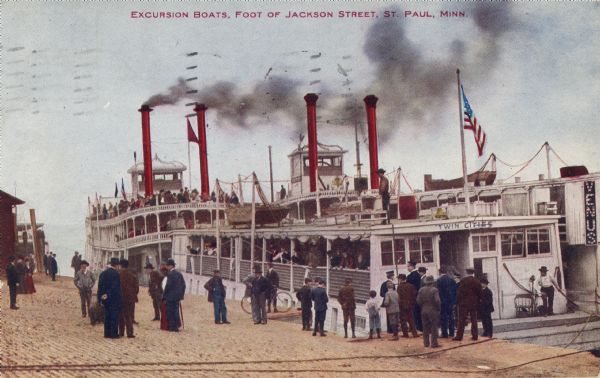 Caption reads: "Excursion Boats, Foot of Jackson Street, St. Paul, Minn." People are standing along the wharf, and crowds of people are on the boats. The boat in the left foreground has a sign that reads: "Twin Cities."