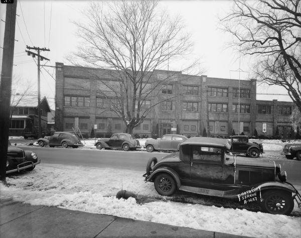 Ray-O-Vac building on the 2300 block of Winnebago Street. Office building and several cars. Snow is on the ground. The sign near the door in the center of the factory building reads: "Ray-O-Vac Employment Office Across Street." A service flag (or banner) is on the right near another entrance.