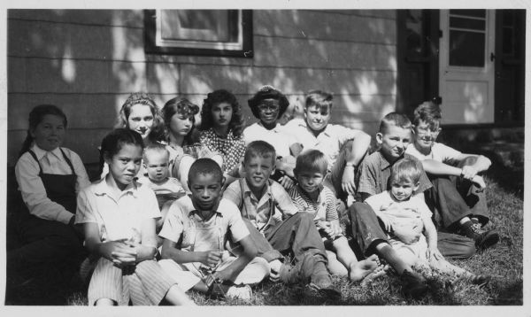 A casual group portrait of children of pacifist families at Fellowship Farm. Written on back: "Back row: Virginia Bright, Jeanine Graham(?) holding Charles Uphoff, Elvere Lutell, Elspeth Gadow, girl from Chicago, Jim — Front: Joan Taliaferro, Calvin Lee Harris, Ralph _ (Iowa), Norman Uphoff, Larry (Iowa) w/Gene Uphoff, _?." "Camp for children of Pacifist families 1945."