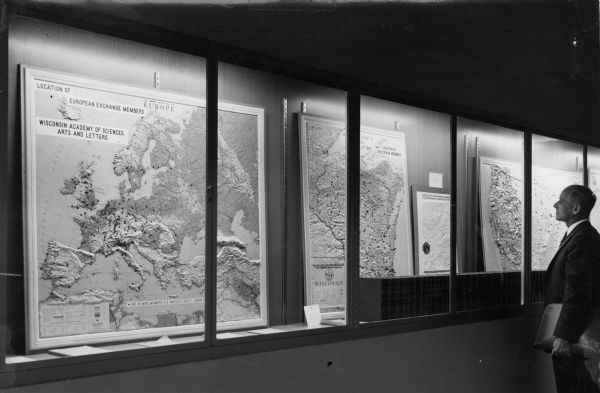 Walter E. Scott views a display arranged by Harold F. Williams showing the locations of Wisconsin members of the Wisconsin Academy of Sciences Arts and Letters. Another display in the foreground indicates the locations of European exchange members of the Academy.
