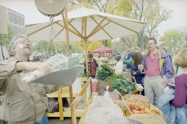 A vendor weighs vegetables for sale at the Dane County Farmers' Market on the Capitol Square. The Wisconsin State Capitol is in the background on the right.