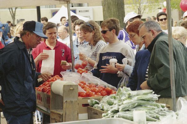 A farmers sells vegetables to customers at the Dane County Farmers' Market on the Capitol Square.