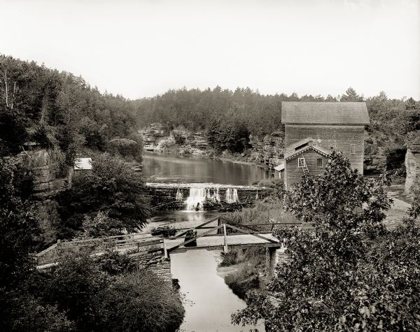 Elevated view of Mirror Lake Mill with bridge in foreground. Two women are standing on the bridge looking down at the river.
