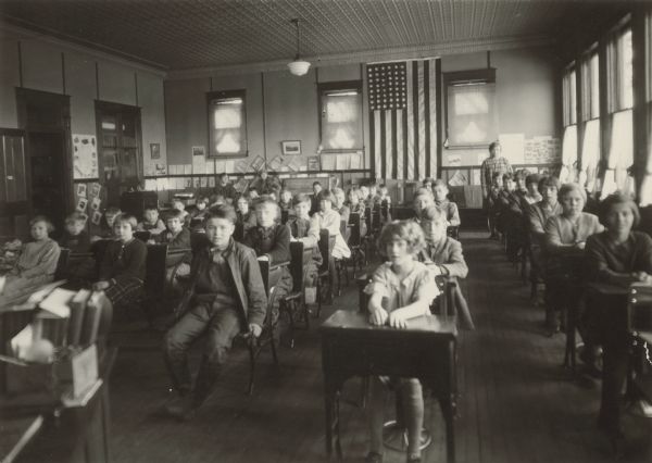 View from front of classroom of students seated at desks at Spring Brook School near Berlin. A woman is standing in the back of the classroom on the right near the windows, and two other women are sitting in the back.