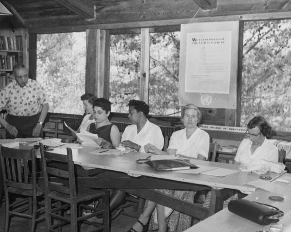 Five women are sitting and one man is standing in the Highlander Library. The UN Charter is displayed behind them.