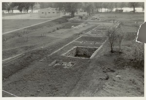 Elevated view of Fort Crawford facing west showing north row of buildings. The Mississippi River is in the background. Typewritten caption reads: "Fort Crawford: facing west showing North row of buildings (including cellar) and North west bastion. Modern swimming pool to the left."