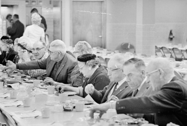 A group of men and women are sitting at a long table together eating fish fry.