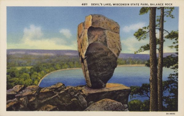 Colorized postcard of Balance Rock, a formation in Devil's Lake State Park. There are carved initials and other markings on the rock formation. A tree is visible to the right and the lake, trees, bluffs and sky are in the background. The text at the top reads: "Devil's Lake, Wisconsin State Park, Balance Rock."