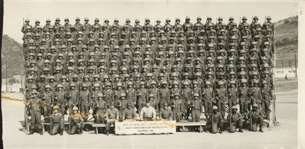 Outdoor group portrait. The sign in front reads: "United States Marine Corps Q Company 2nd Battalion, 2nd Infantry Training Regiment Camp Pendleton California, November 1968." Note accompanying photograph reads: "5th row 6 from the left."