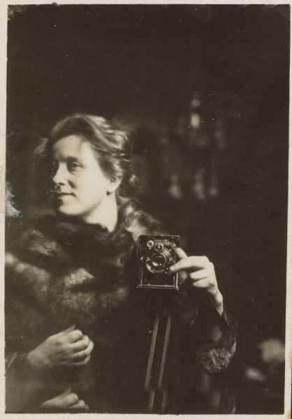 Sigrid Schultz holding a camera on a tripod. She is likely taking a self-portrait in a mirror.