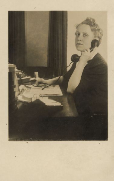 Sigrid Schultz pauses to look at the camera while talking on the telephone.