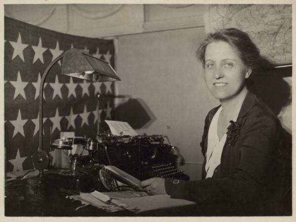 Sigrid Schultz poses at a desk with a typewriter and a telephone. 