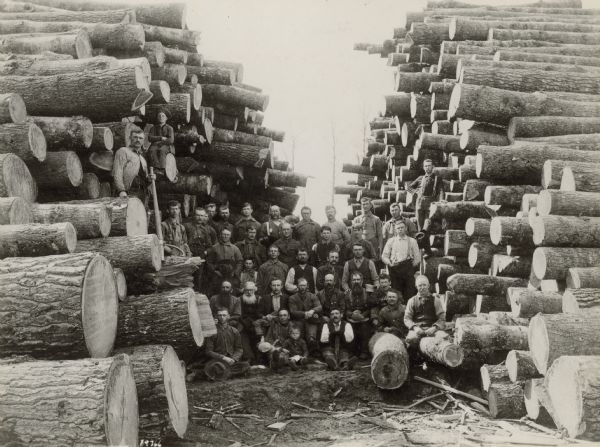 Loggers posed between two large stacks of logs near Antigo, perhaps the camp of D. Sulivan.