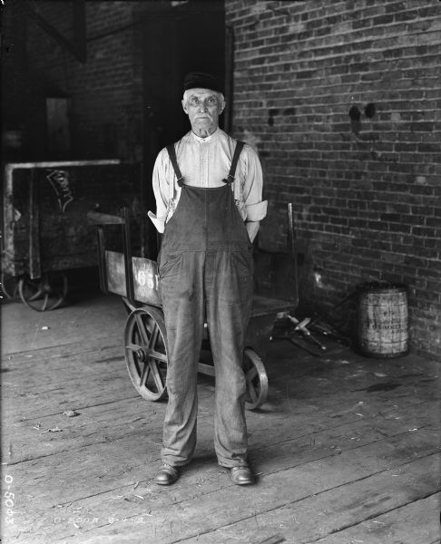 A man is standing on a loading dock. Carts are behind him next to the door of a brick factory building.