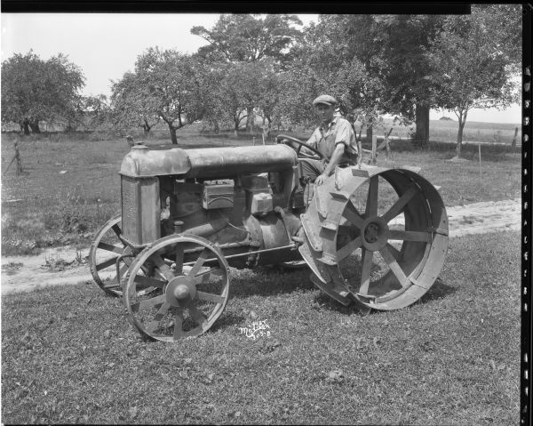 Left side view of a man sitting on a Fordson tractor, which has extra rims.