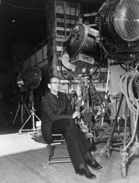 Robert Bloch sitting on a film set, likely "Straight Jacket," surrounded by film equipment.