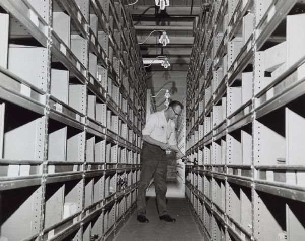 Shipping clerk checking bins. Caption reads: "Computer Even Plots Route to Bins — Speedier shipment is assured by the system's ability to locate requested parts and indicates to shipping clerk the best route for picking order."