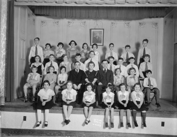Group portrait of Jewish children and teachers sitting on a stage in the Workmen's Circle Labor Lyceum, 41 - 43 N. Mills Street at Spring Street, Greenbush. They are going to present a Jewish play "Chanukah Money."