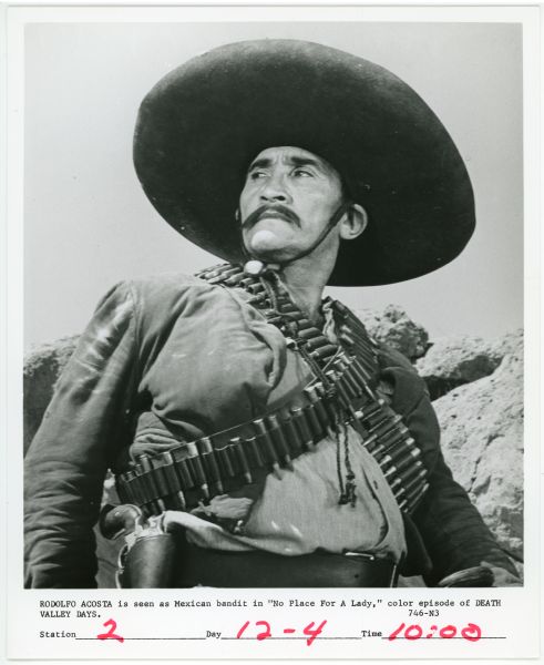 Publicity photograph of Rodolfo Acosta in a scene from the TV show <i>Death Valley Days</i>.  Acosta plays a Mexican bandit and has two bandoliers full of bullets strapped across his chest.