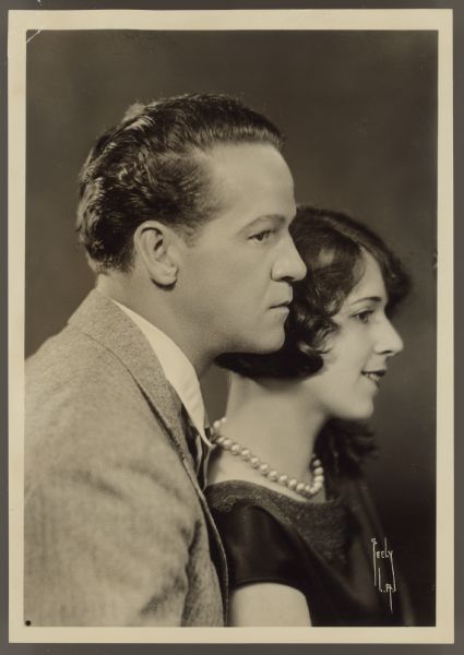 Photograph of movie stars, and real life couple, Helen Ferguson and William Russell.  The couple sit in profile to the camera with Ferguson in front of Russell. 