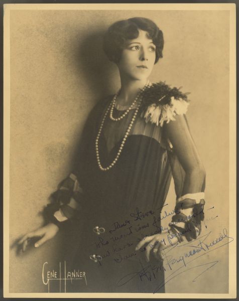Photograph of actress Helen Ferguson posing next to a wall and looking over her shoulder.  She wears a dark colored dress with sheer arms and top.  There is an adornment on the top of one shoulder and at the bottom of both sleeves.  She is also wearing a double strand of pearls necklace.  There is a handwritten inscription to Dan and Steve in the bottom right corner.