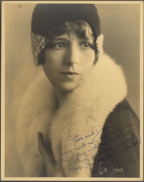 Actress Helen Ferguson poses for a photograph wearing a hat and coat with fur trim.  She looks to the side and her hat covers her head except for her bangs.  One hand can be seen at the opening of the coat.  There is a handwritten inscription to Steve and Dan at the bottom right of the photograph.