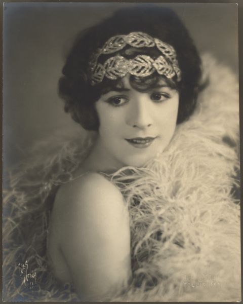 Actress Helen Ferguson wears a very large feather boa in a portrait along with a sparkly leaf shaped headpiece.