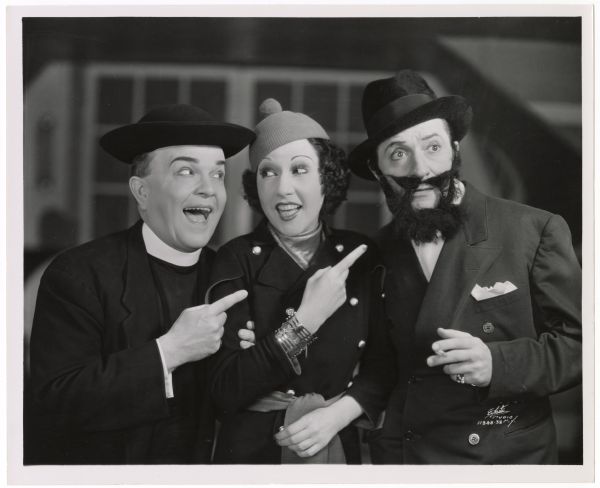Ethel Merman, Victor Moore and William Gaxton in the musical <i>Anything Goes</i>.  Merman and Moore smile and look at each other while they both point at Gaxton who wears a fake beard and has a worried look on his face.  Moore is dressed as a minister.