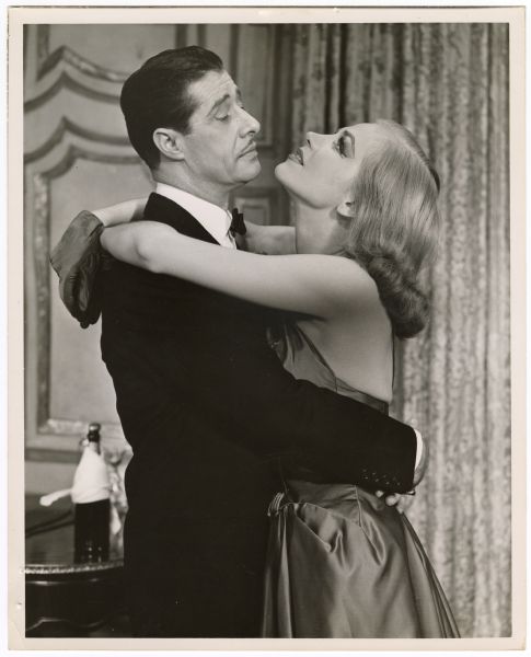 Actors Don Ameche and Hildegarde Neff embrace one another during the play <i>Silk Stockings</i>. Both are dressed in formal wear. Ameche looks at Neff who looks toward the ceiling.