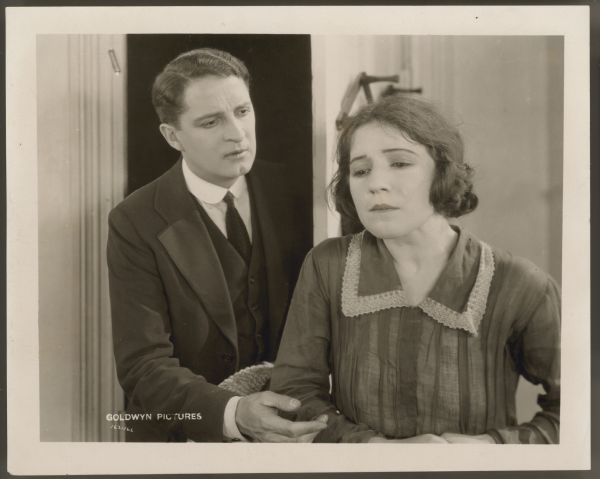 Bryant Washburn stands in a doorway and reaches for Helen Ferguson in a scene from the 1922 film <i>Hungry Hearts</i>.  Ferguson has her back to him and is crying.